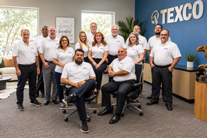 Texco team of professionals posing together in a modern office, wearing matching white polo shirts.