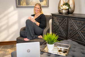 Woman relaxing in armchair with coffee cup and HP laptop on ottoman in stylish home office setting.