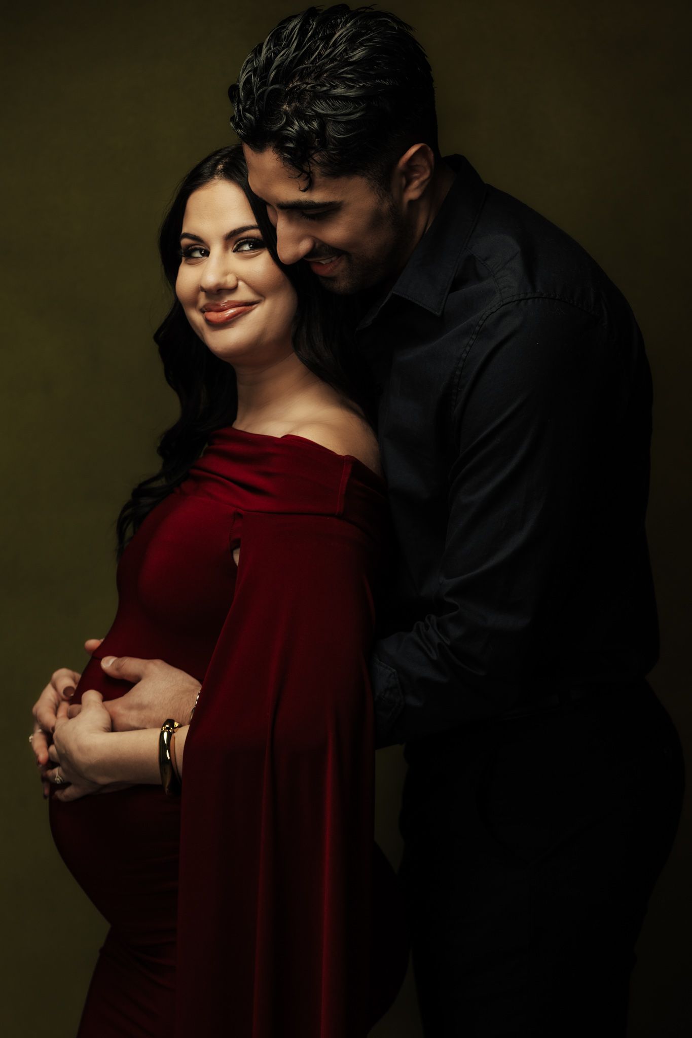 Couple embraces tenderly, with woman in red dress against moody dark background.