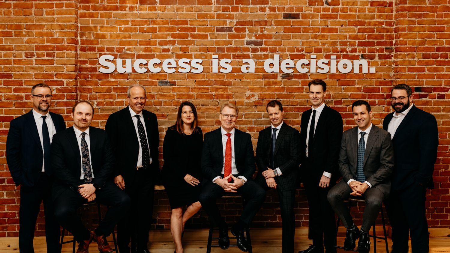 Business professionals pose in front of a brick wall with text reading 'Success is a decision' above them.
