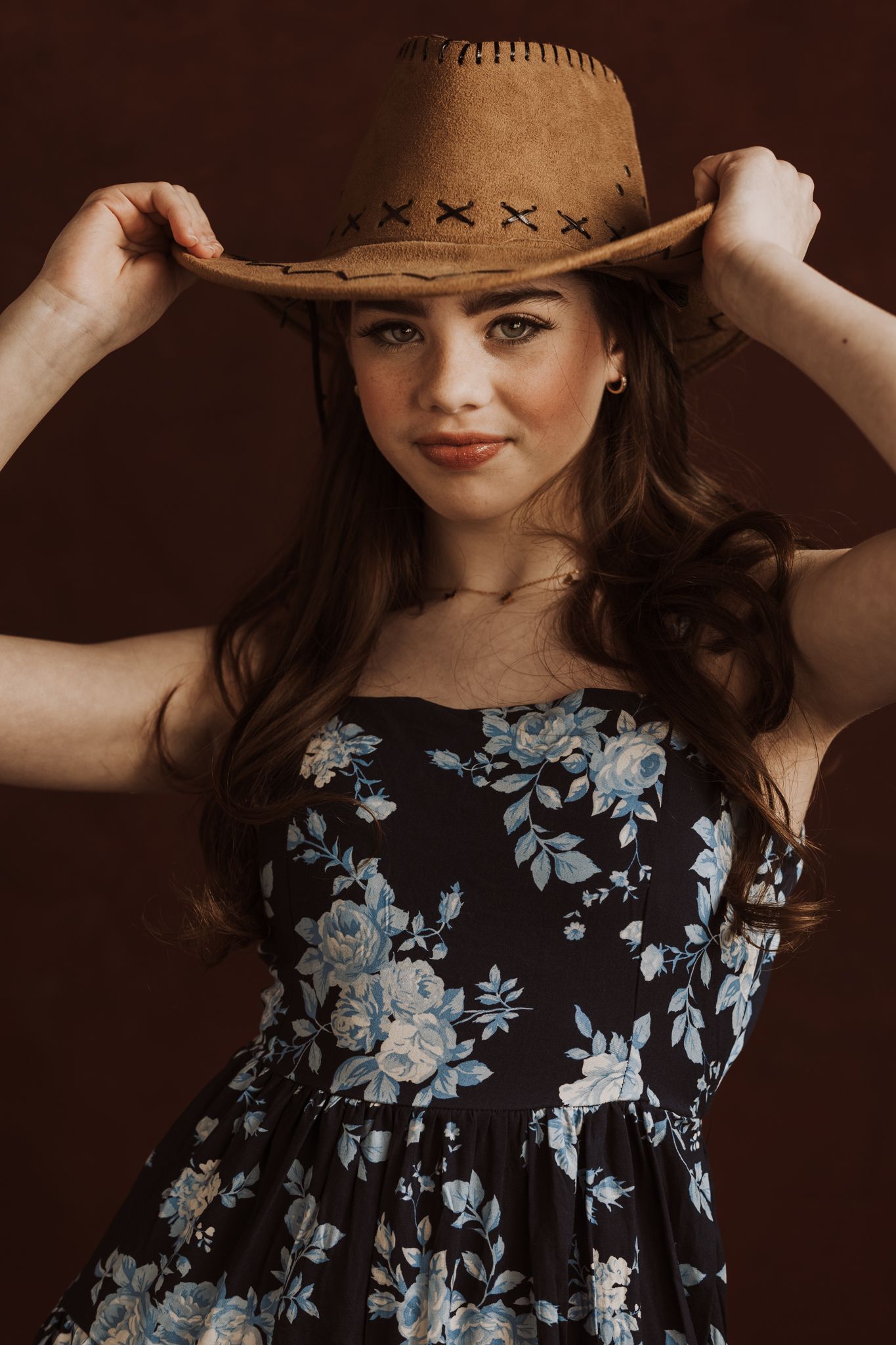 Fashion portraits wearing cowboy hat and floral dress against sepia backdrop.