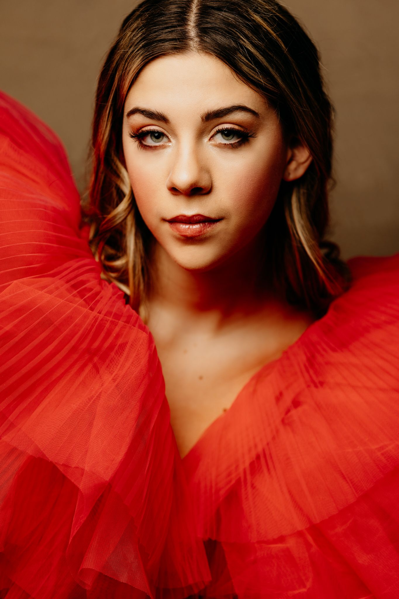 Fashion portrait in dramatic red tulle gown against dark background.