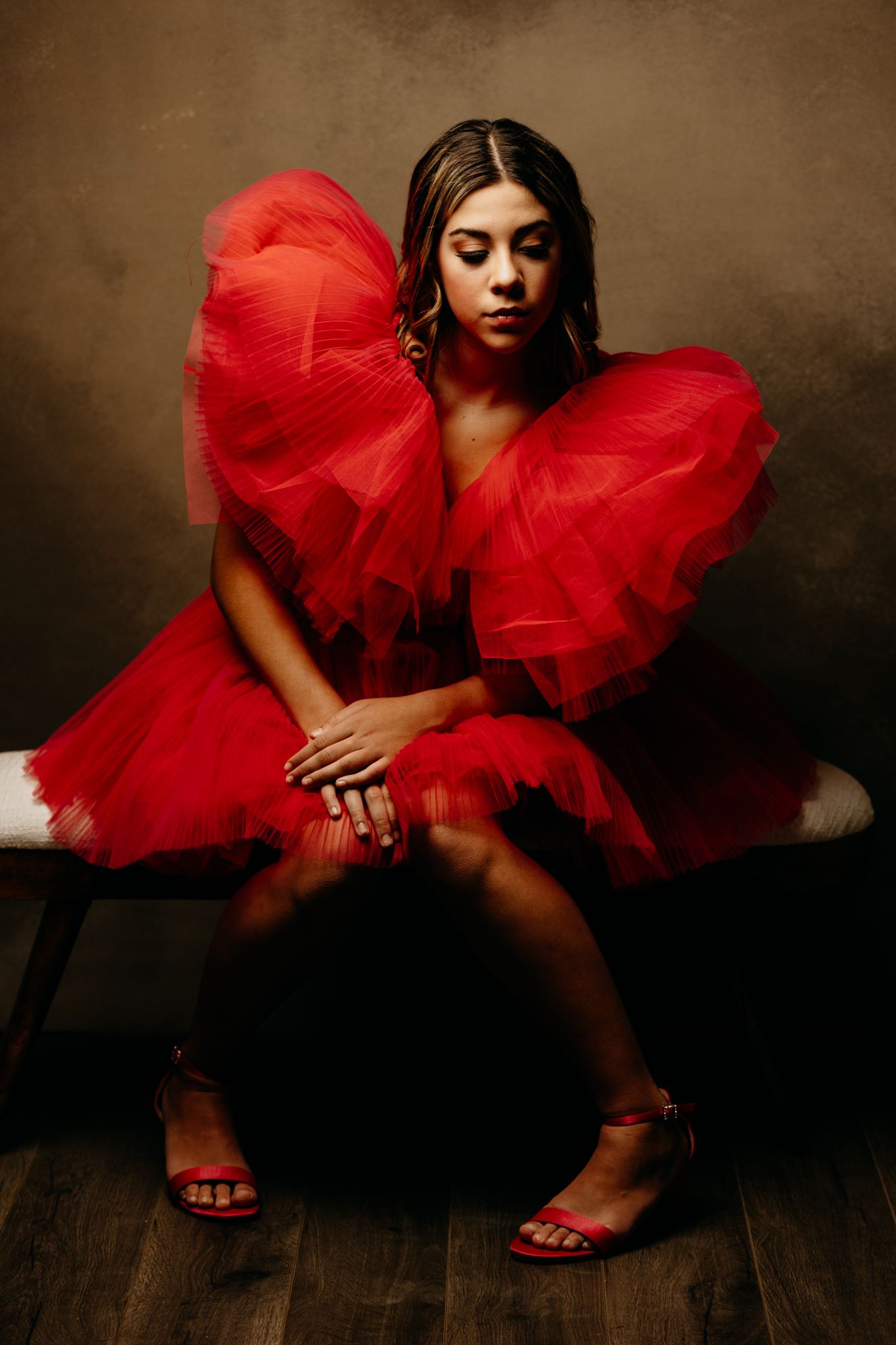 Artistic photo series showing model in flowing red tulle dress on dark floor.
