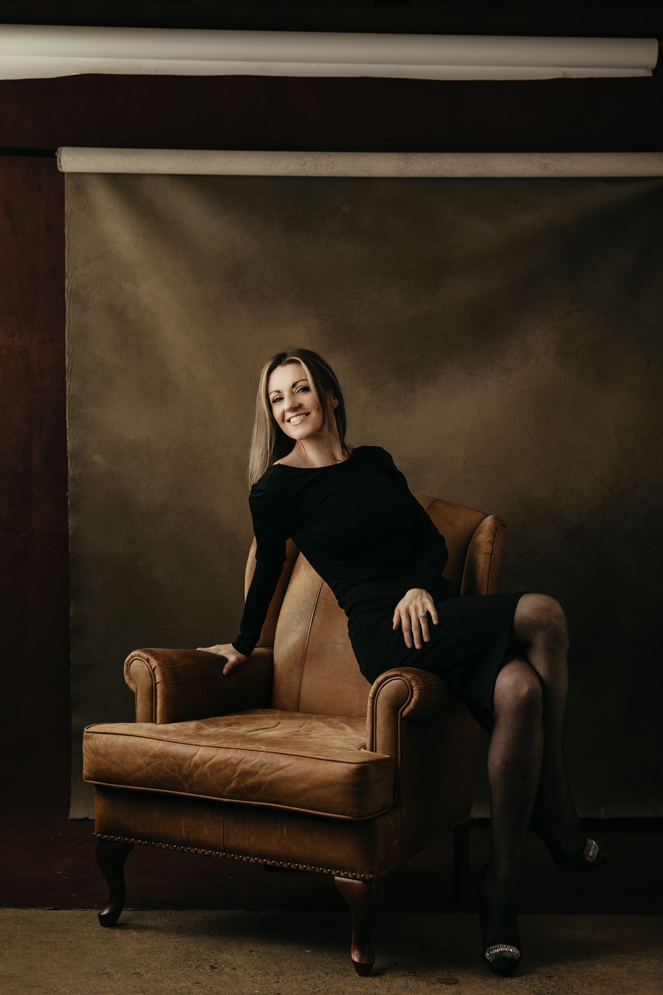 Artistic portrait on vintage brown leather chair with moody lighting.
