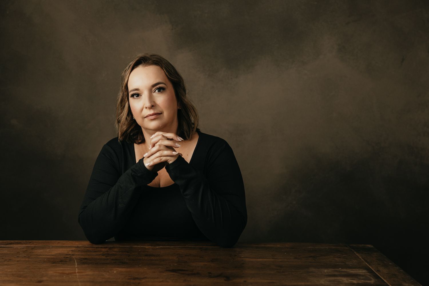 Dramatic portrait at wooden table with moody lighting and dark background.