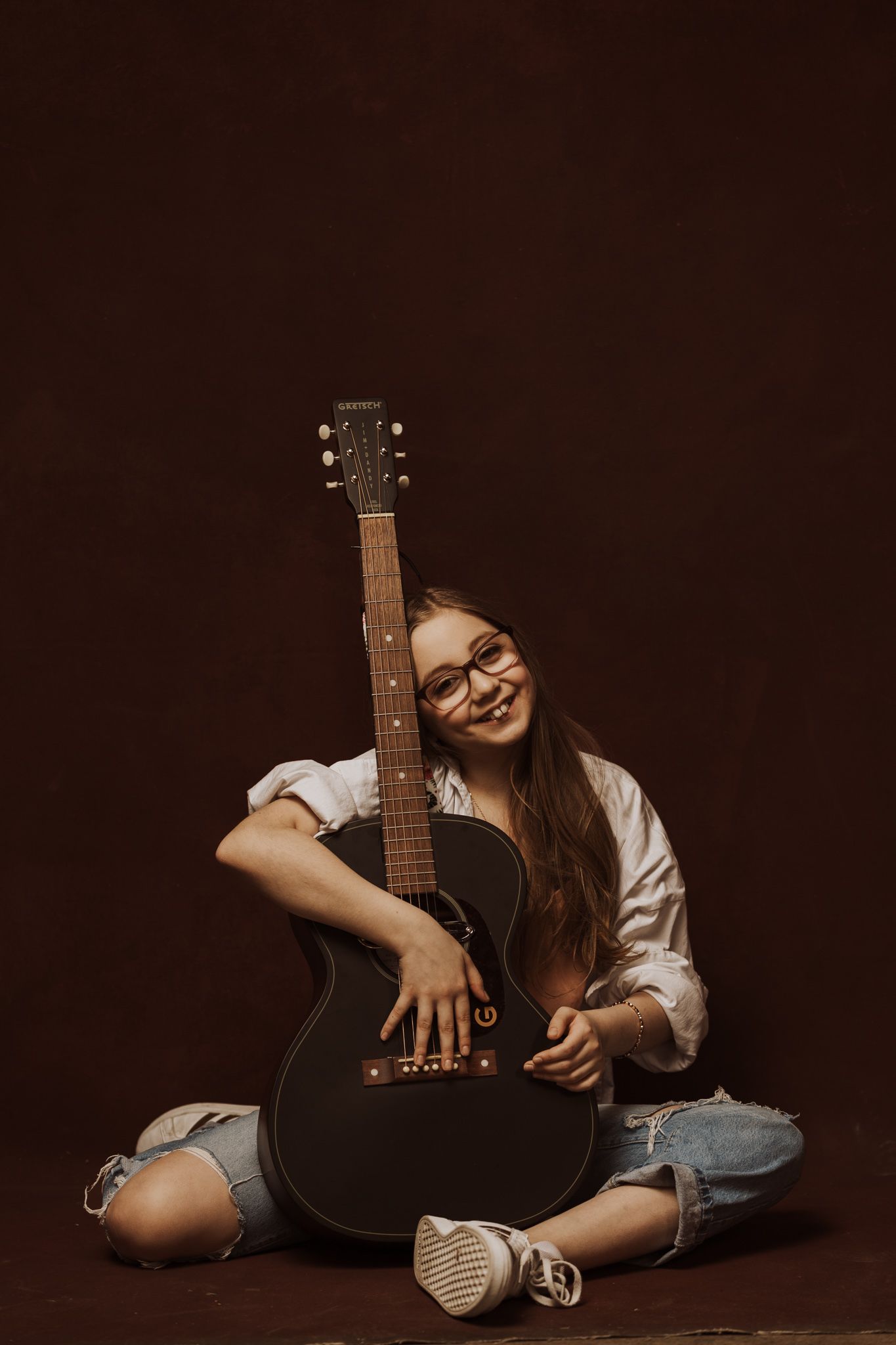 A musician poses with an acoustic guitar in a series of artistic studio portraits against a dark background.