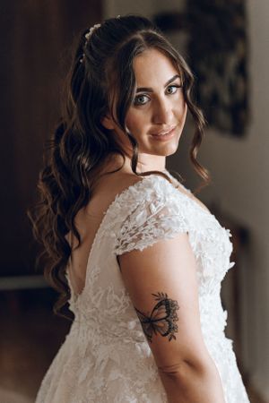 Close-up portrait of bride in lace gown with butterfly tattoo and flowing curls.