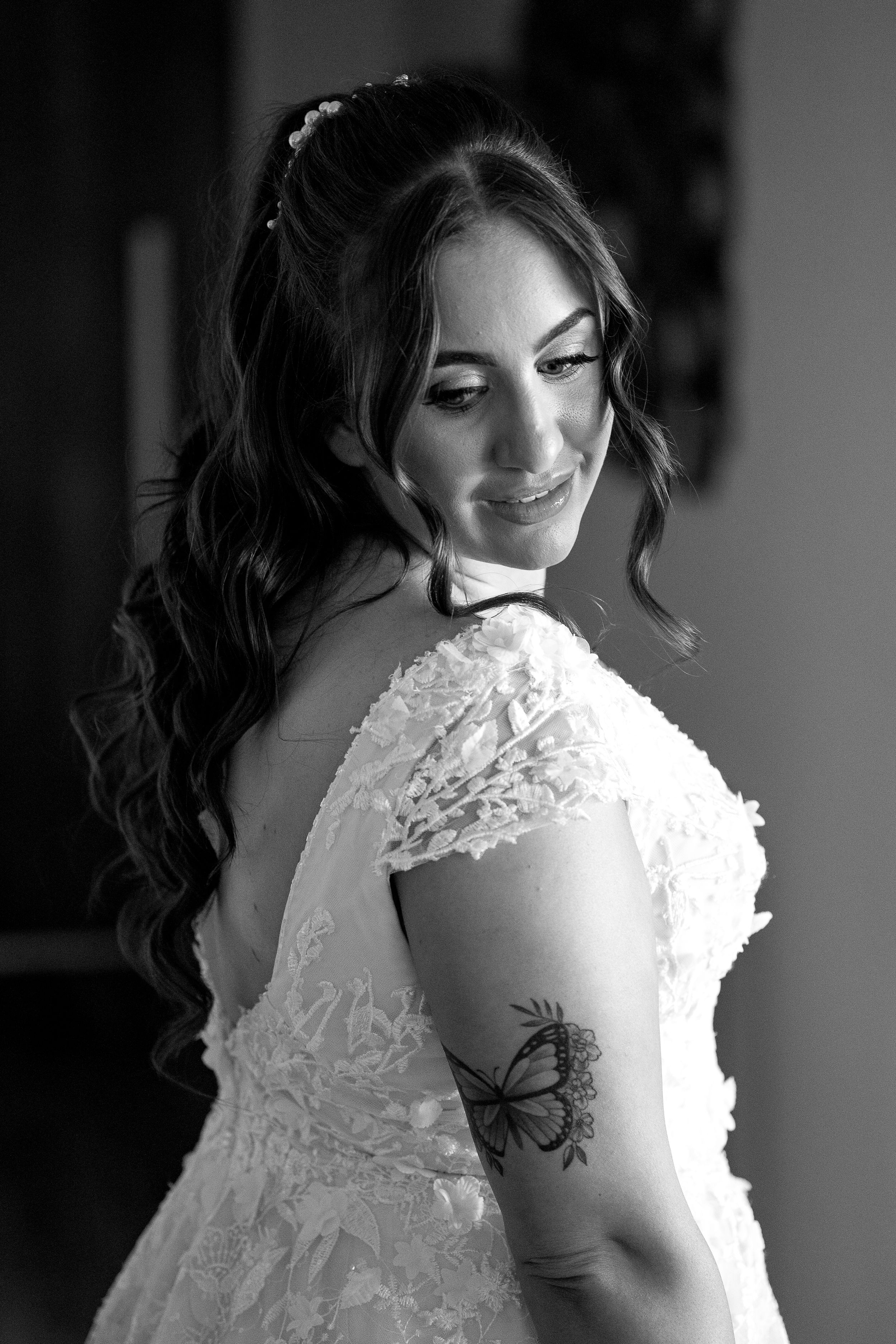 Black and white portrait of bride in lace dress showing butterfly tattoo on arm.