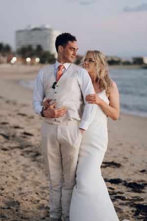 Newlyweds sharing an intimate moment on a beach at sunset.