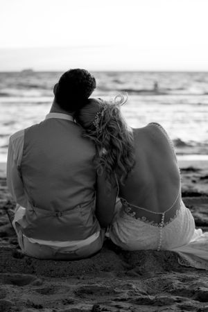 Romantic silhouette of couple sitting together on beach watching ocean waves.