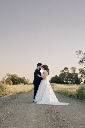 Sunset wedding portrait of couple embracing on rural dirt road.