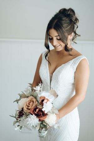 Bride holds romantic bouquet of blush and white flowers against white backdrop.