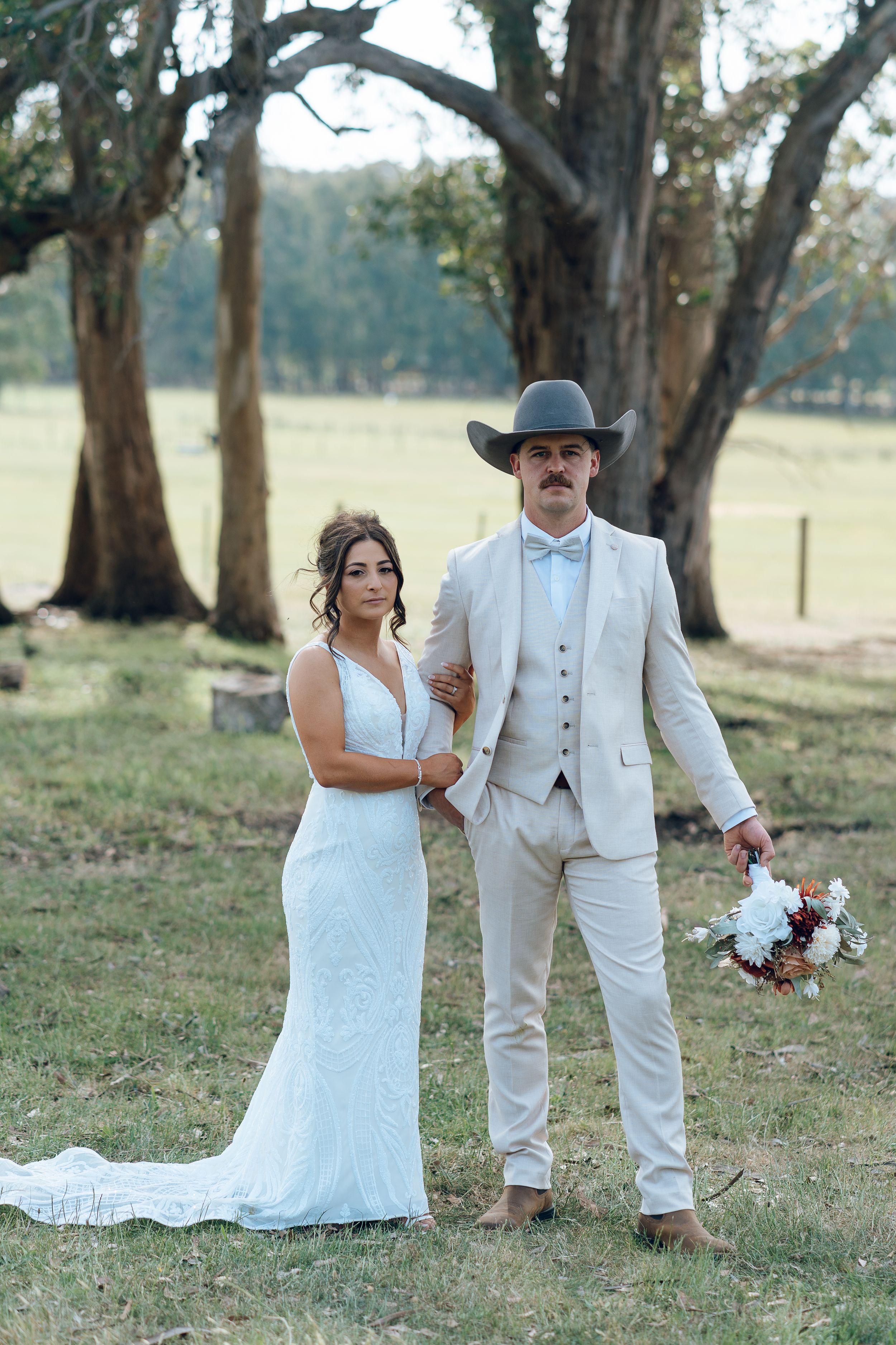 Elegant country wedding portrait with couple in white attire and cowboy hat.