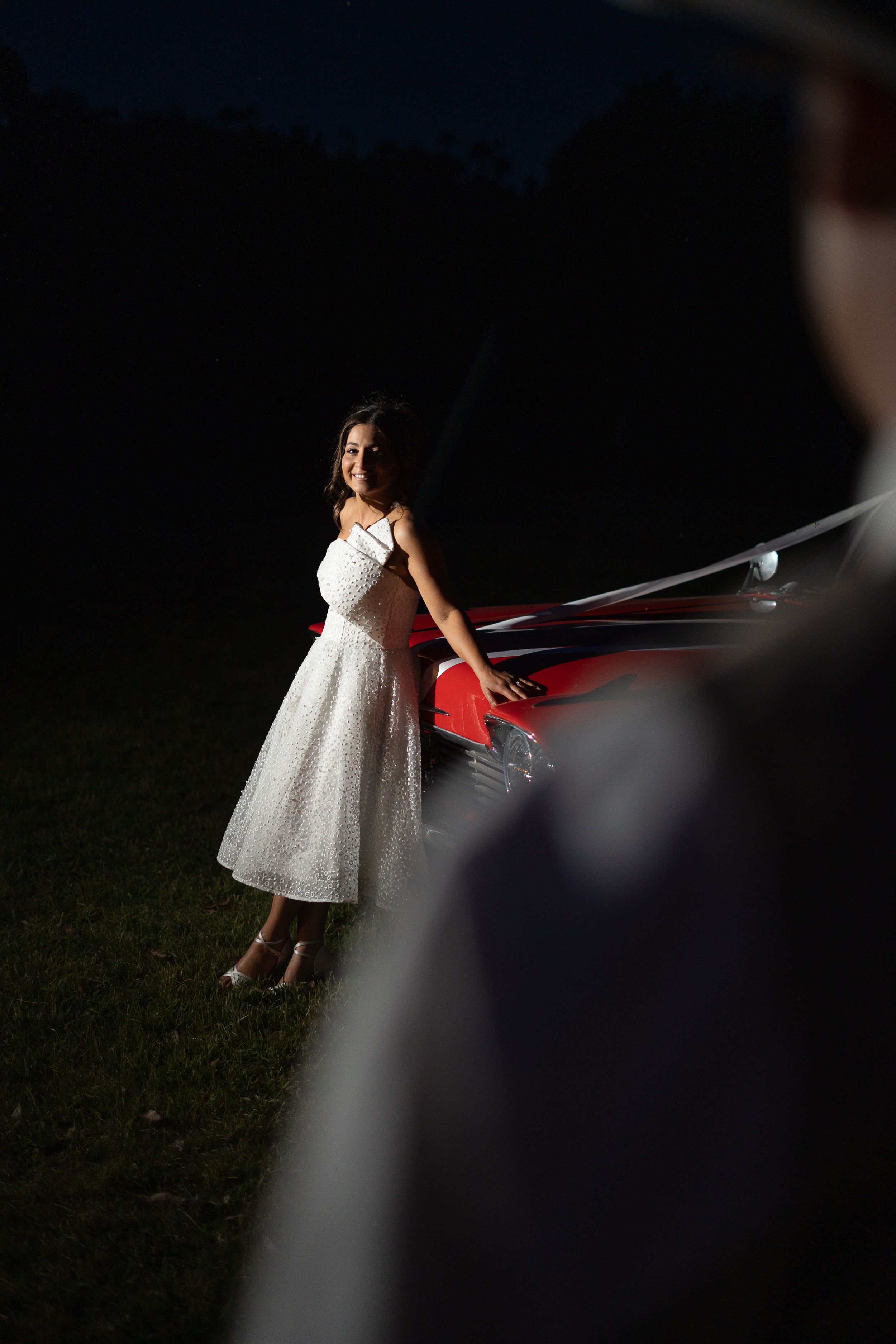 Artistic night portrait of bride in tea-length dress by car.