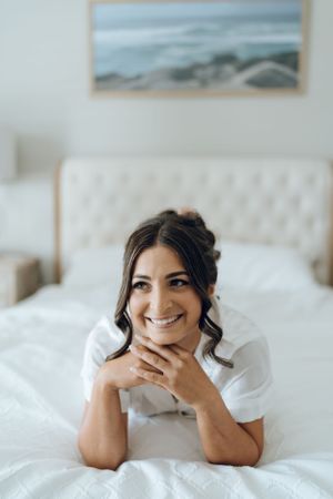 Woman lying on white bedding in a bright room with natural lighting.