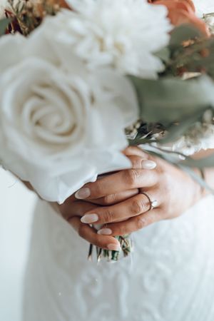 Close-up of hands holding white roses against a light background.