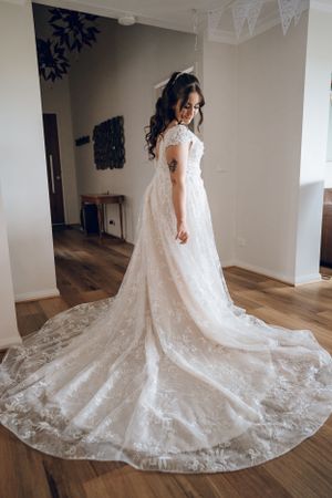 Full-length view of lace wedding gown with dramatic cathedral train on hardwood floor.