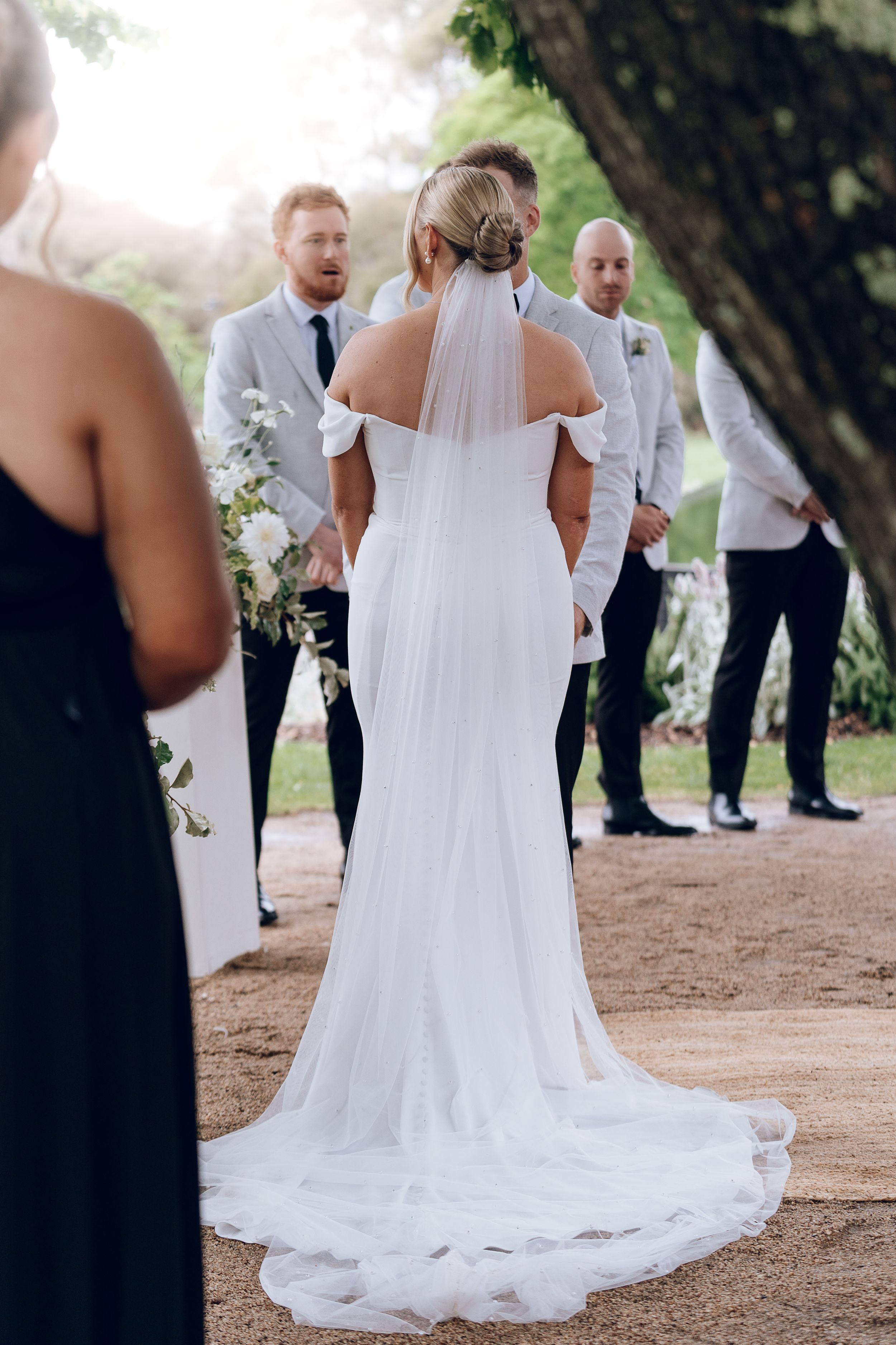 Back view of bride in flowing wedding gown with train during outdoor ceremony.