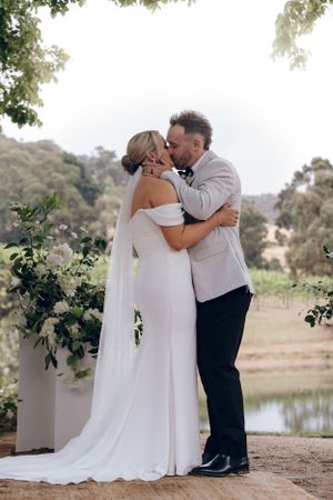 Romantic wedding kiss in front of floral arch with lake view.