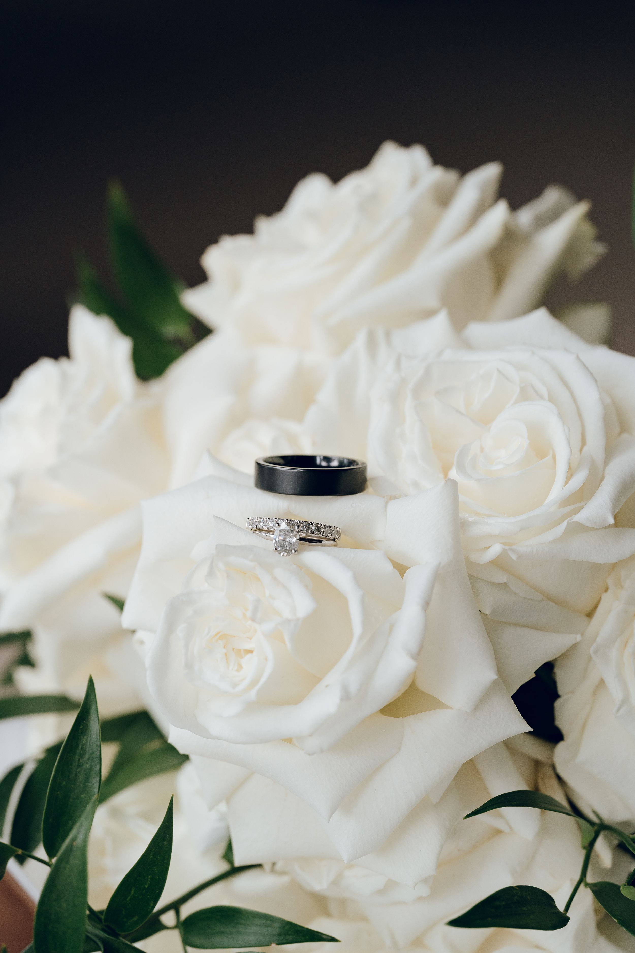 Wedding rings nestled among white roses and greenery.