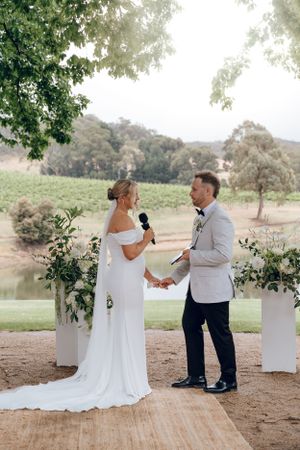 Outdoor wedding ceremony takes place with floral columns and scenic vineyard backdrop.