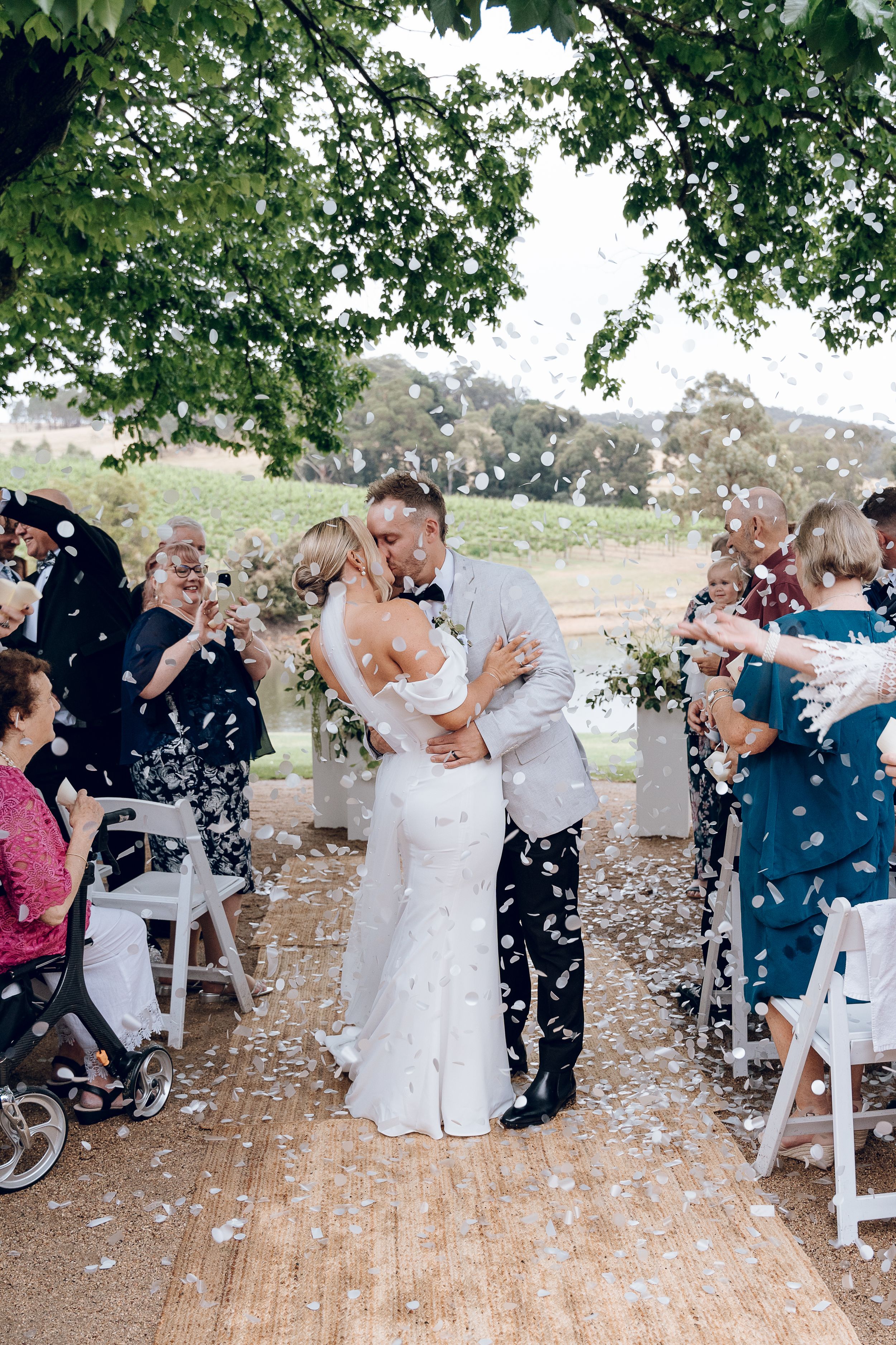 Wedding guests throw confetti during recessional on rustic outdoor platform.