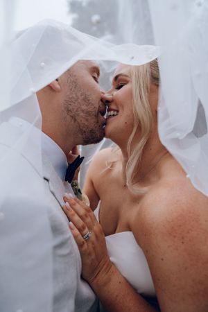 Intimate moment shared under bridal veil during wedding celebration.