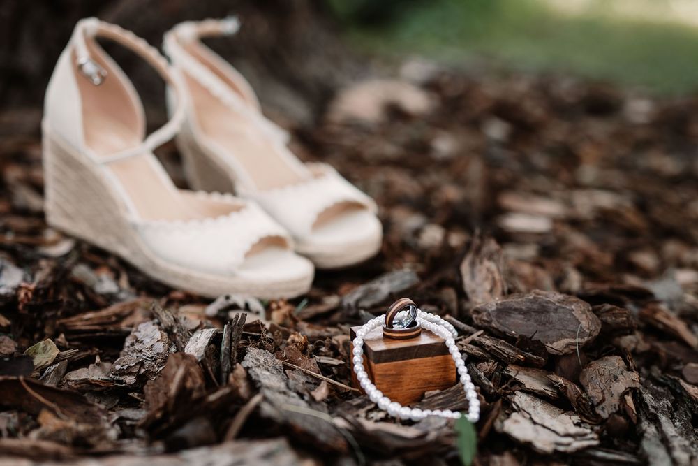 Rows of scattered rose gold wedding shoes displayed among rustic leaves and branches create an artistic nature-inspired arrangement.