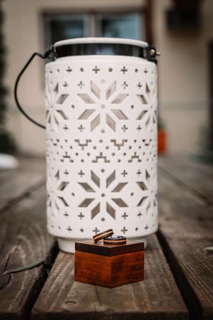 White ceramic lantern with intricate snowflake cutout pattern sits on rustic wooden surface in soft lighting.