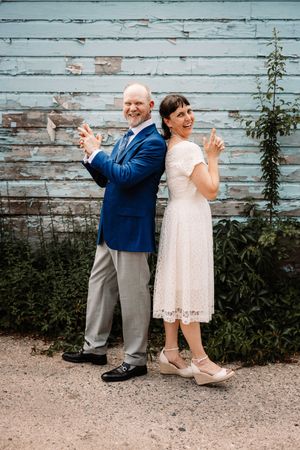 A couple in wedding attire poses playfully against a rustic blue wooden wall for a series of fun dance-inspired photos.