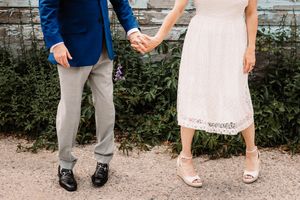 Wedding couple and guests show off their shoes in a line against a stone wall background.