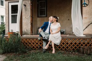 A person wearing a white dress sits on a porch railing while another stands nearby at an outdoor venue.