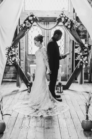 Black and white wedding photo of couple standing back-to-back under floral arch.
