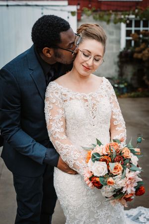 Tender moment captured between newlyweds with coral and white floral bouquet.