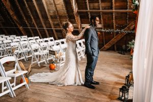 Wedding couple holds hands in rustic barn venue with white folding chairs.