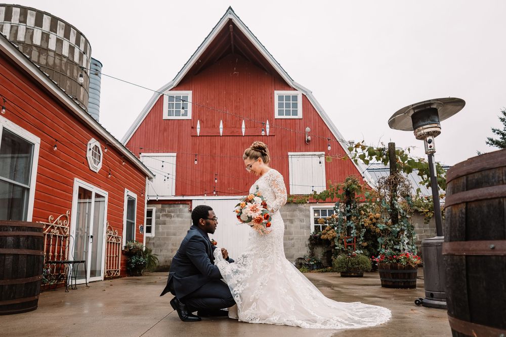 Wedding proposal scene in front of red barn with person kneeling.