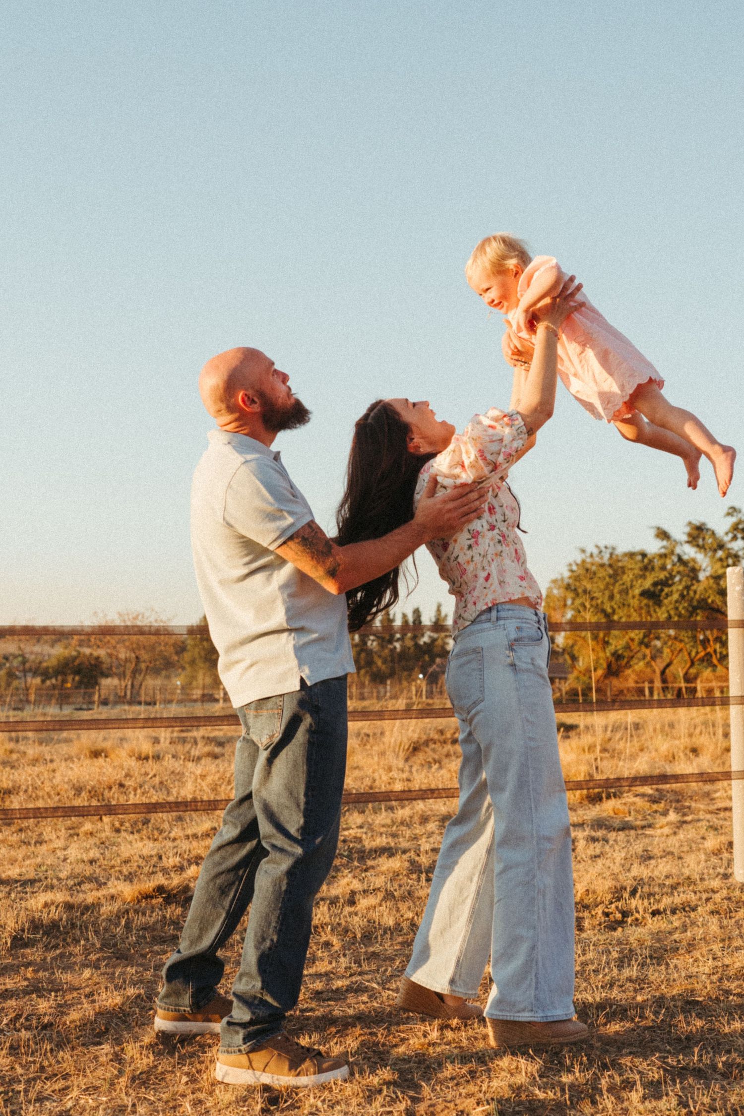 A family playing and lifting their child in the air during sunset in an open field.