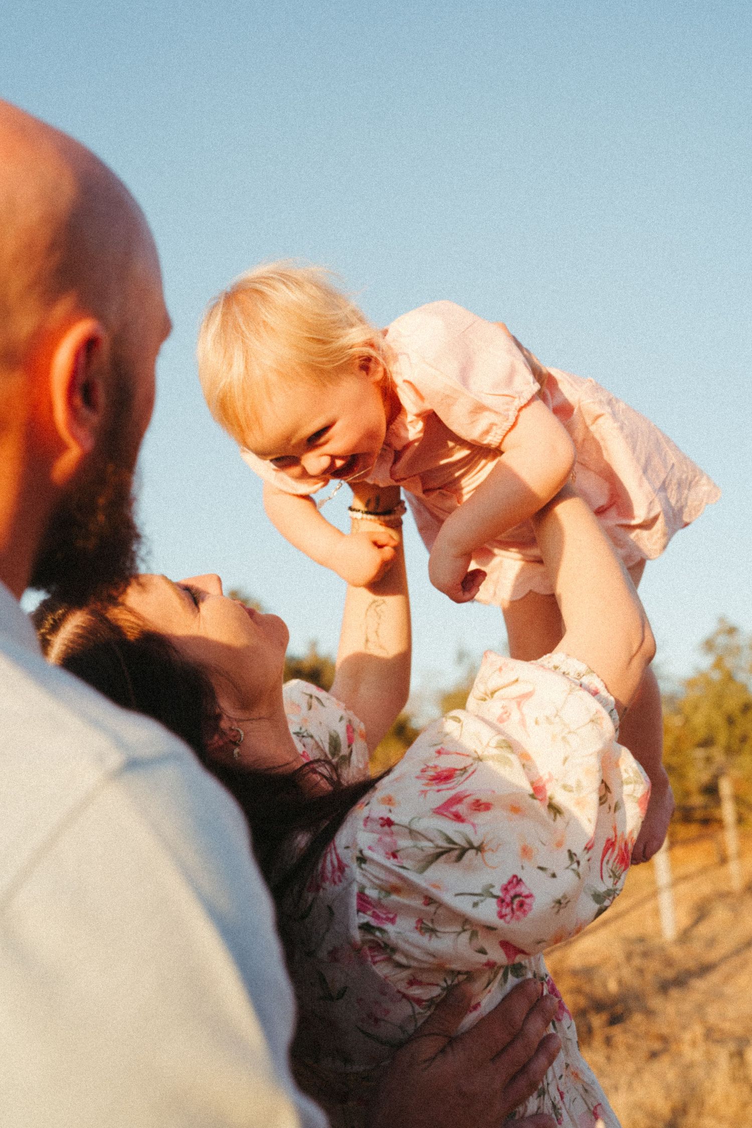 A joyful family moment captured during sunset as they lift their baby in the air.
