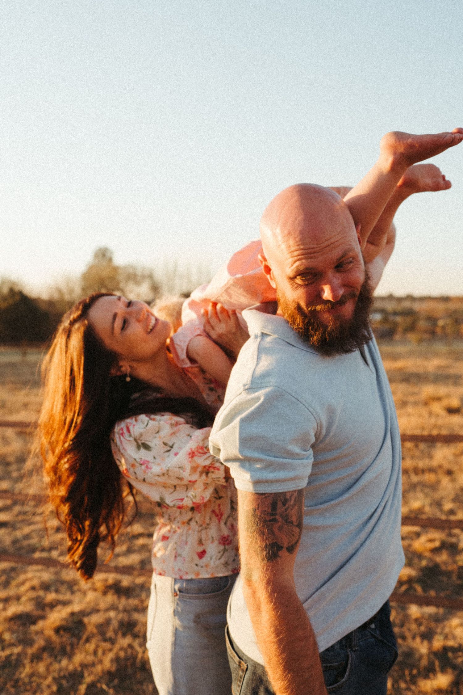 A playful family moment captured during golden hour in a rural field.