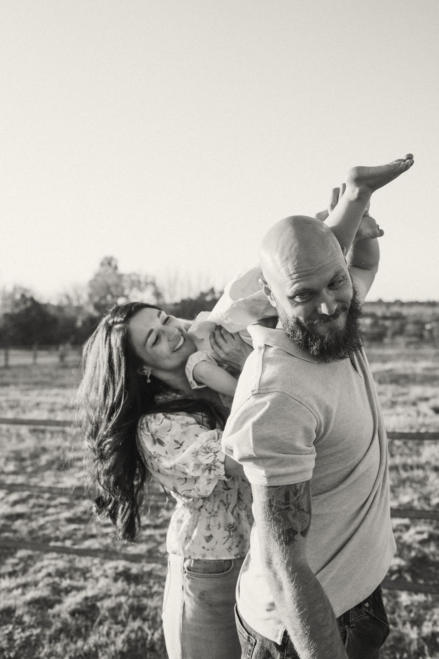A black and white photo capturing a playful family moment in an outdoor field.