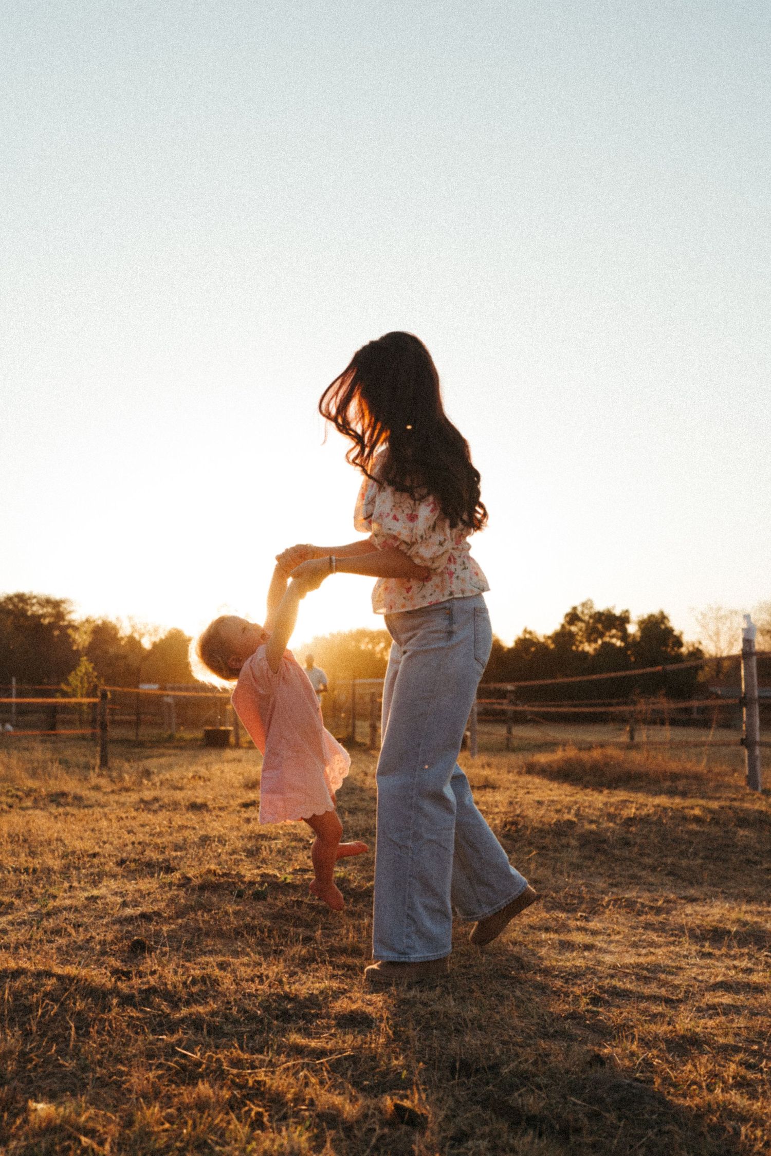 Two figures dance playfully in a golden field at sunset, creating silhouettes against the warm evening light.