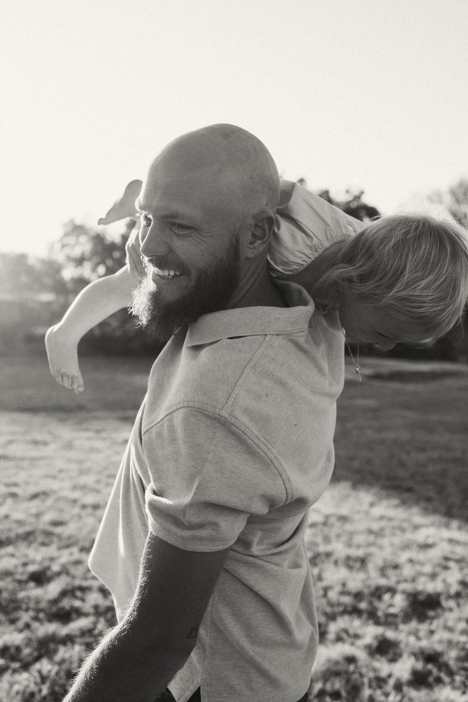 Playful embrace captured in black and white during golden hour in an open field.