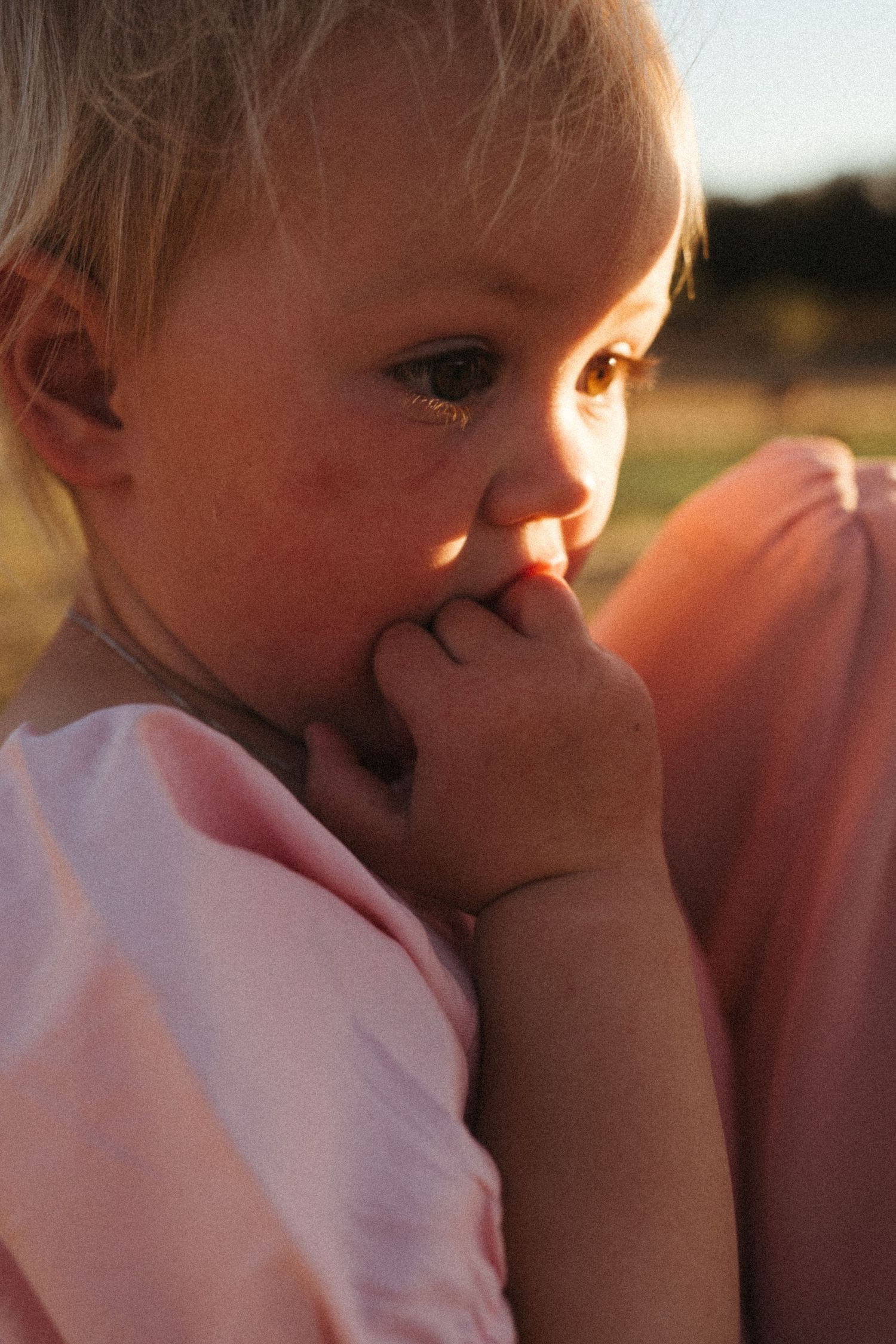 Close-up of small child with hands near face during sunset.