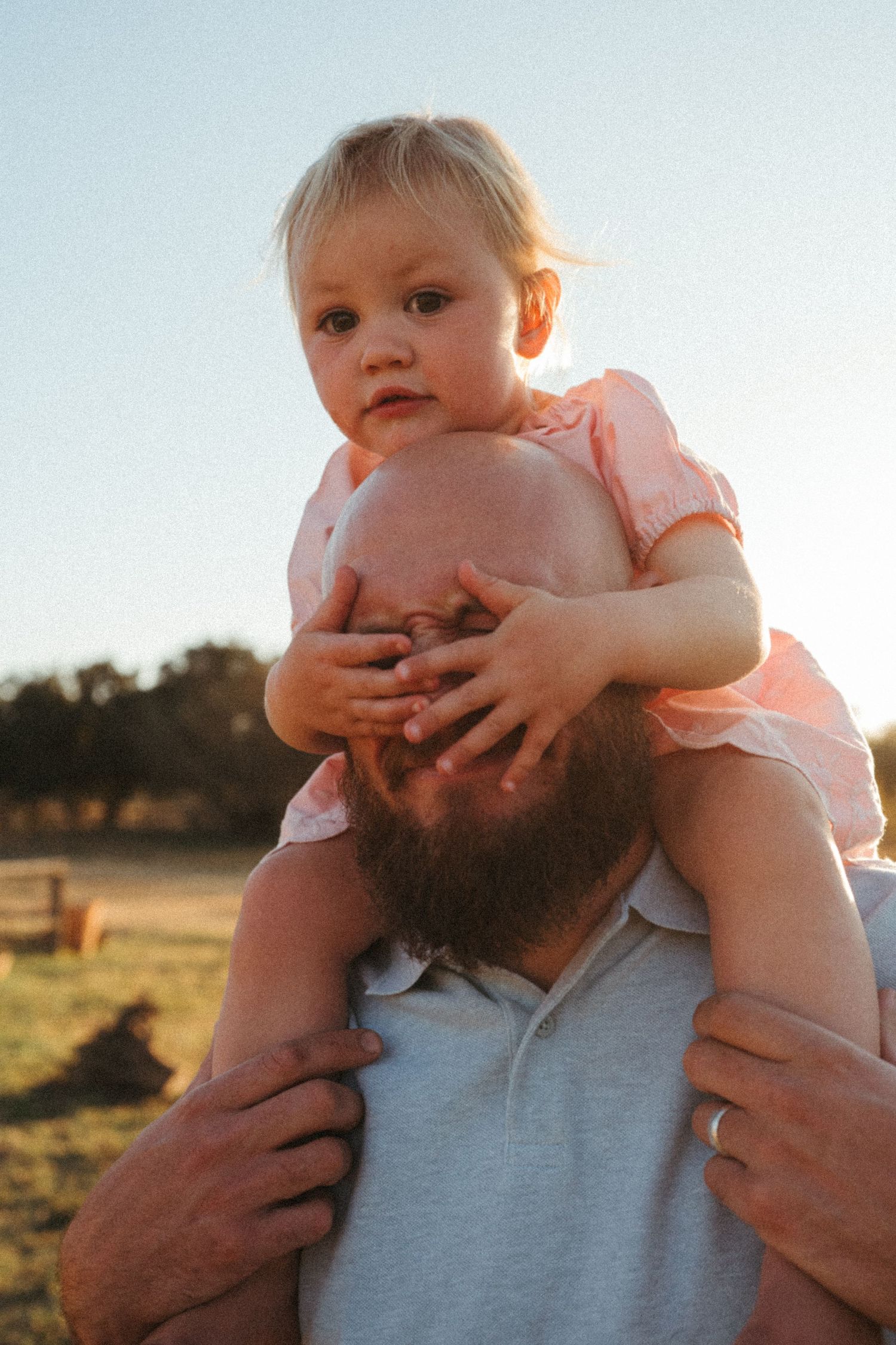 Toddler playfully covering adult's face during outdoor photo session at sunset.