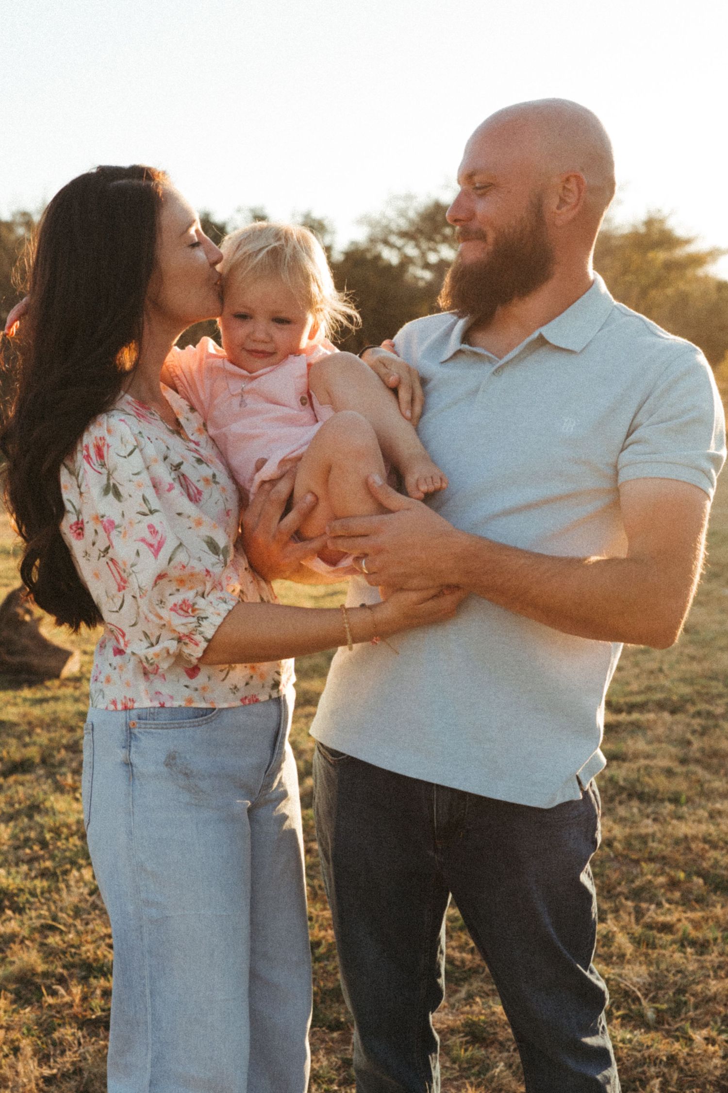 Family of three sharing intimate moments in casual attire during sunset photo session.