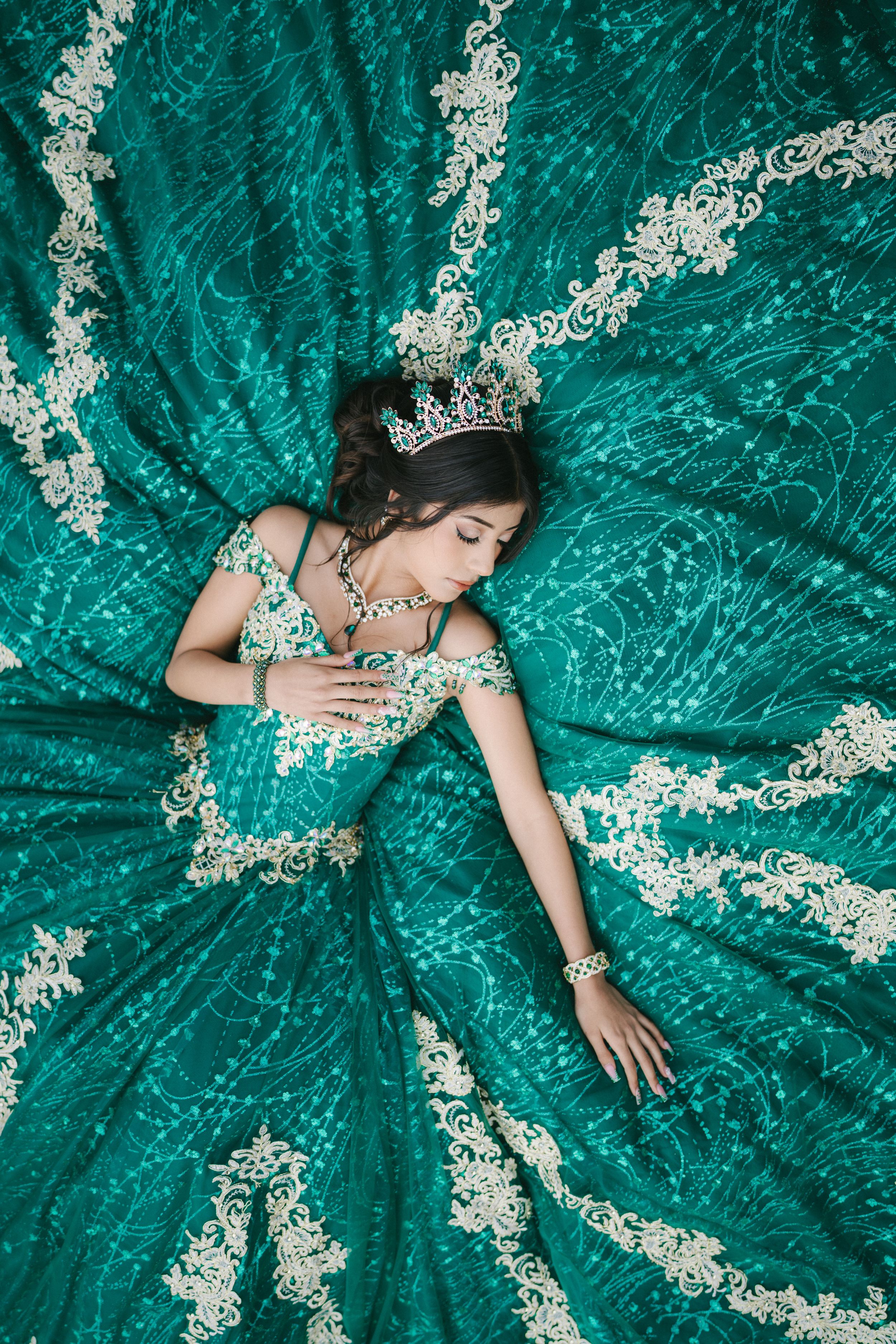 Overhead view of an elegant emerald green ball gown with intricate white lace details spread out in a circular pattern.