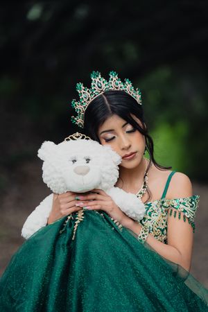 Person wearing elegant emerald green gown poses with white plush teddy bear in series of romantic outdoor photos.