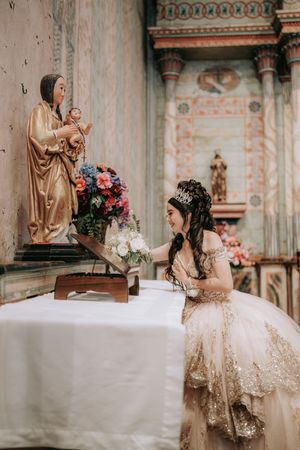 A spiritual moment captured in a church with ornate decor, floral arrangements and religious statuary on display.