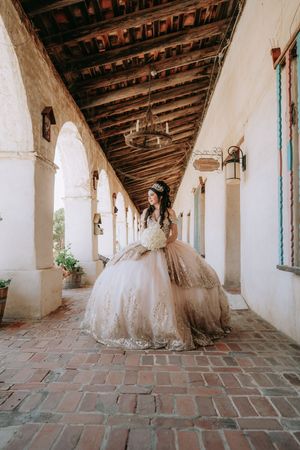 Elegant wedding dress displayed in a covered Spanish colonial style walkway with historic brick floors and white arches.