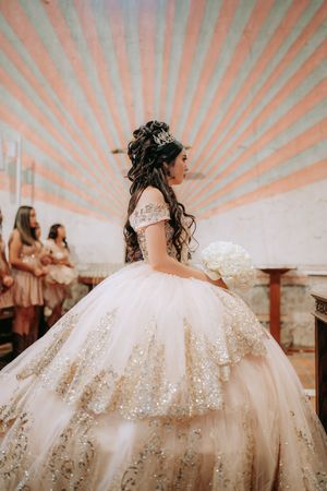 A bride in a luxurious white ball gown with glittering embellishments twirls during a quinceañera celebration.